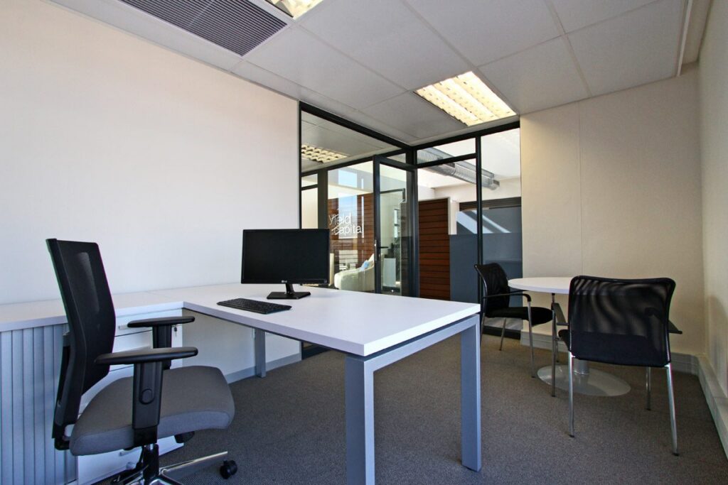 A white L shaped desk with a mesh back chair in a glass fronted office at Yield Capital, by Nuwave