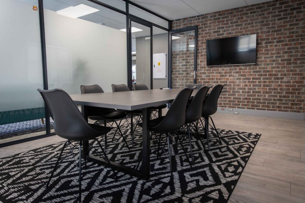 A steel framed boardroom table with black chairs on a patterned rug at Vancula Agency, by Nuwave